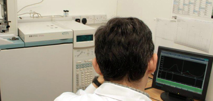 A developer seen from behind reading a graph on a small computer screen, with pieces of paper on the wall and a machine beside him.