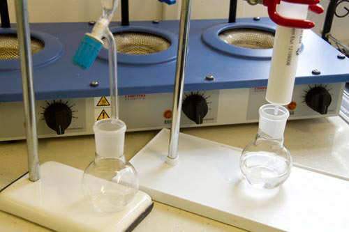 Two conical flasks set up for an experiment in a lab, with containers suspended above them, allowing liquid to drip into the flasks.