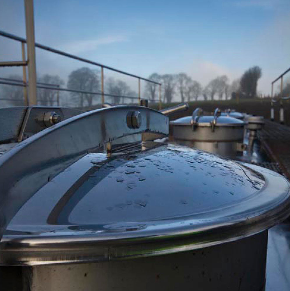 Small metal silos set up in a line on the roof of a building. They are surrounded by a walkway and railings.