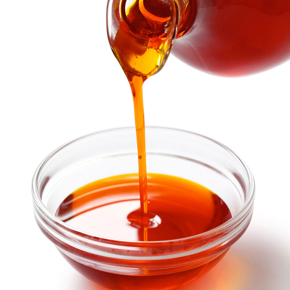 Palm oil pouring from a large bottle into a small glass bowl.